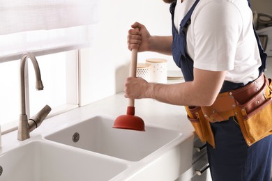 Photo of Plumber using plunger to unclog sink drain in kitchen, closeup