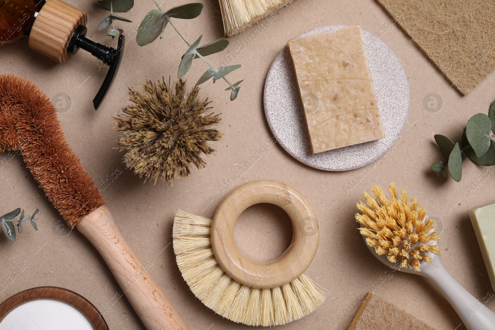 Photo of Cleaning brushes, soap, sponge and eucalyptus leaves on pale brown background, flat lay