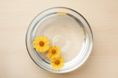 Photo of Glass bowl with water and yellow flowers on wooden table, top view