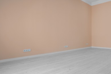 Photo of Pale orange walls with power outlet sockets in empty room