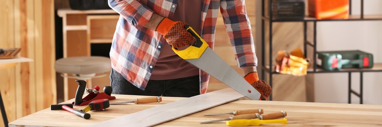 Image of Carpenter sawing wooden plank at table in workshop, closeup. Banner design