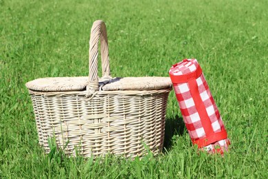 Photo of Rolled checkered tablecloth near picnic basket on green grass outdoors