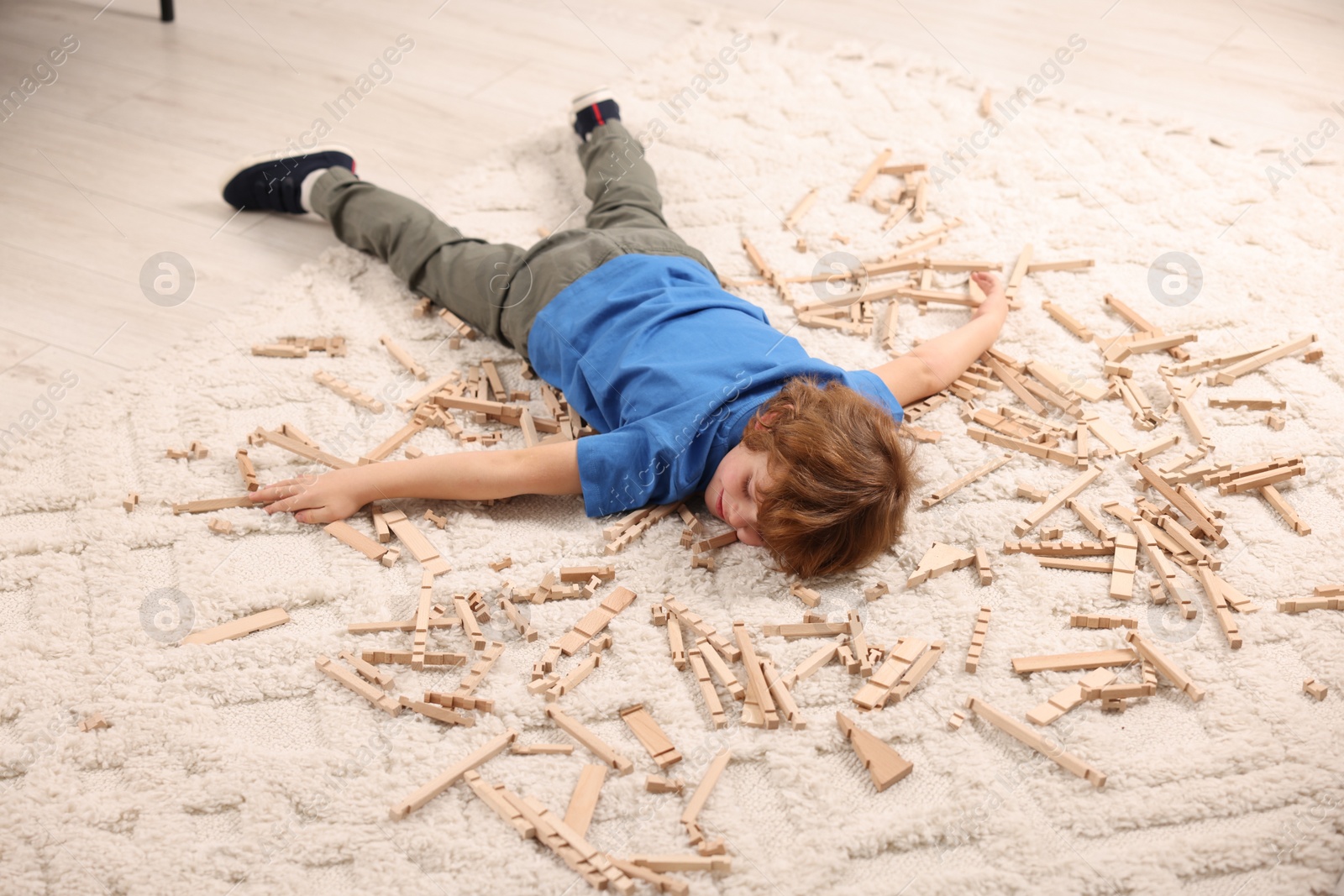 Photo of Little boy surrounded by wooden construction set on carpet at home. Child`s toy