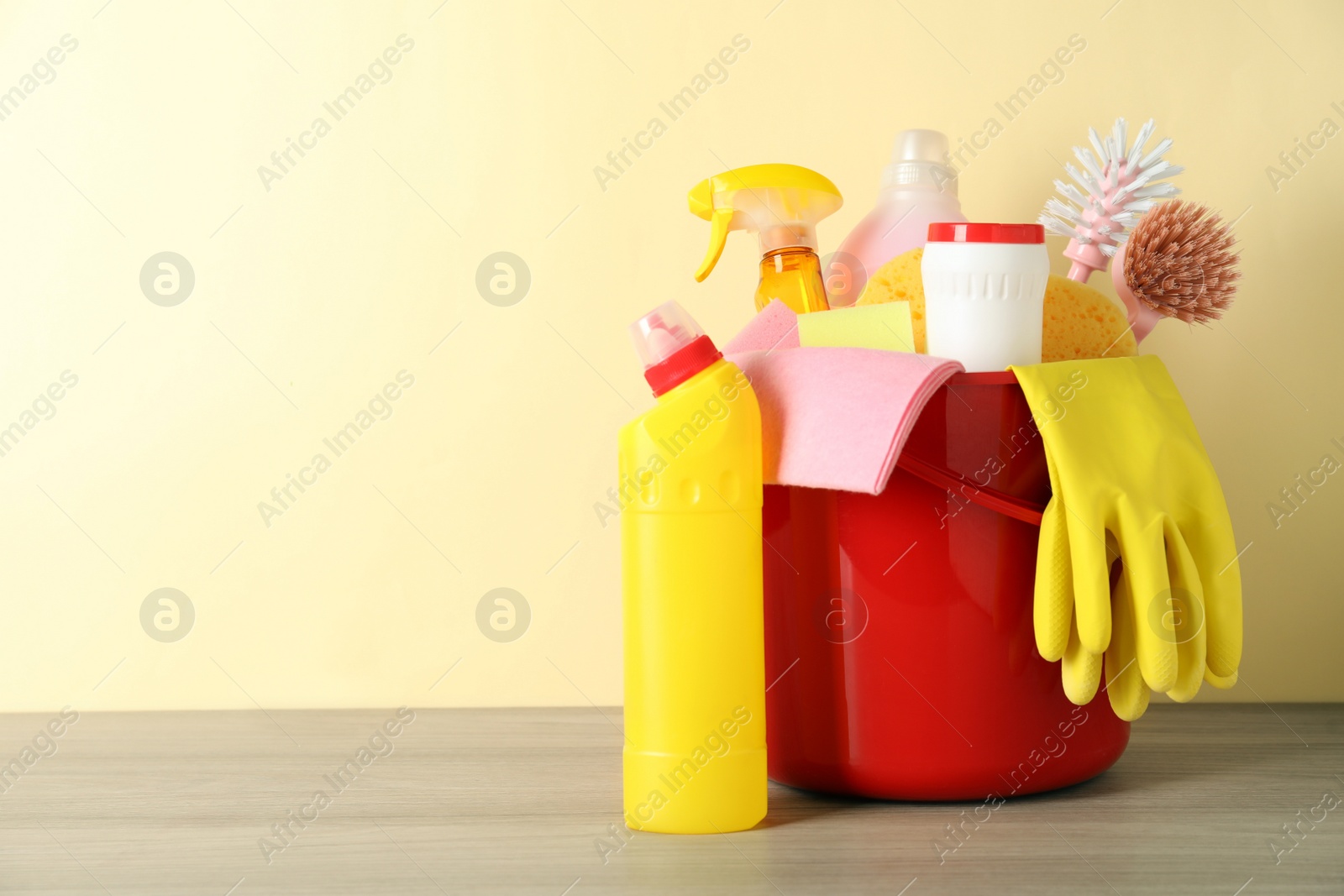 Photo of Bucket with different cleaning supplies on wooden floor near beige wall