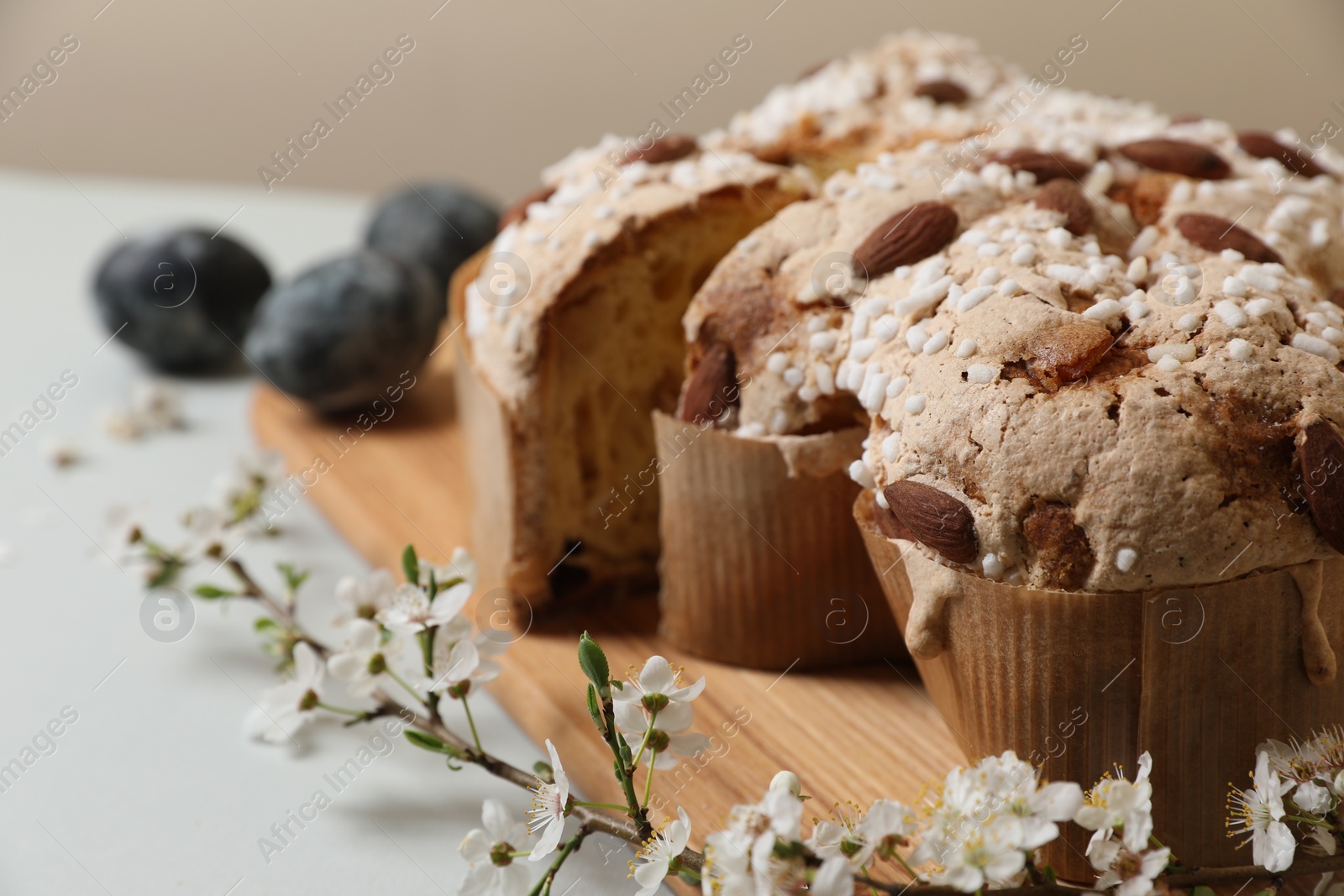 Photo of Pieces of delicious Italian Easter dove cake (traditional Colomba di Pasqua), branch with flowers and painted eggs on light grey table, closeup