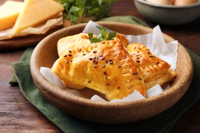 Photo of Fresh delicious puff pastry with cheese in bowl on wooden table, closeup