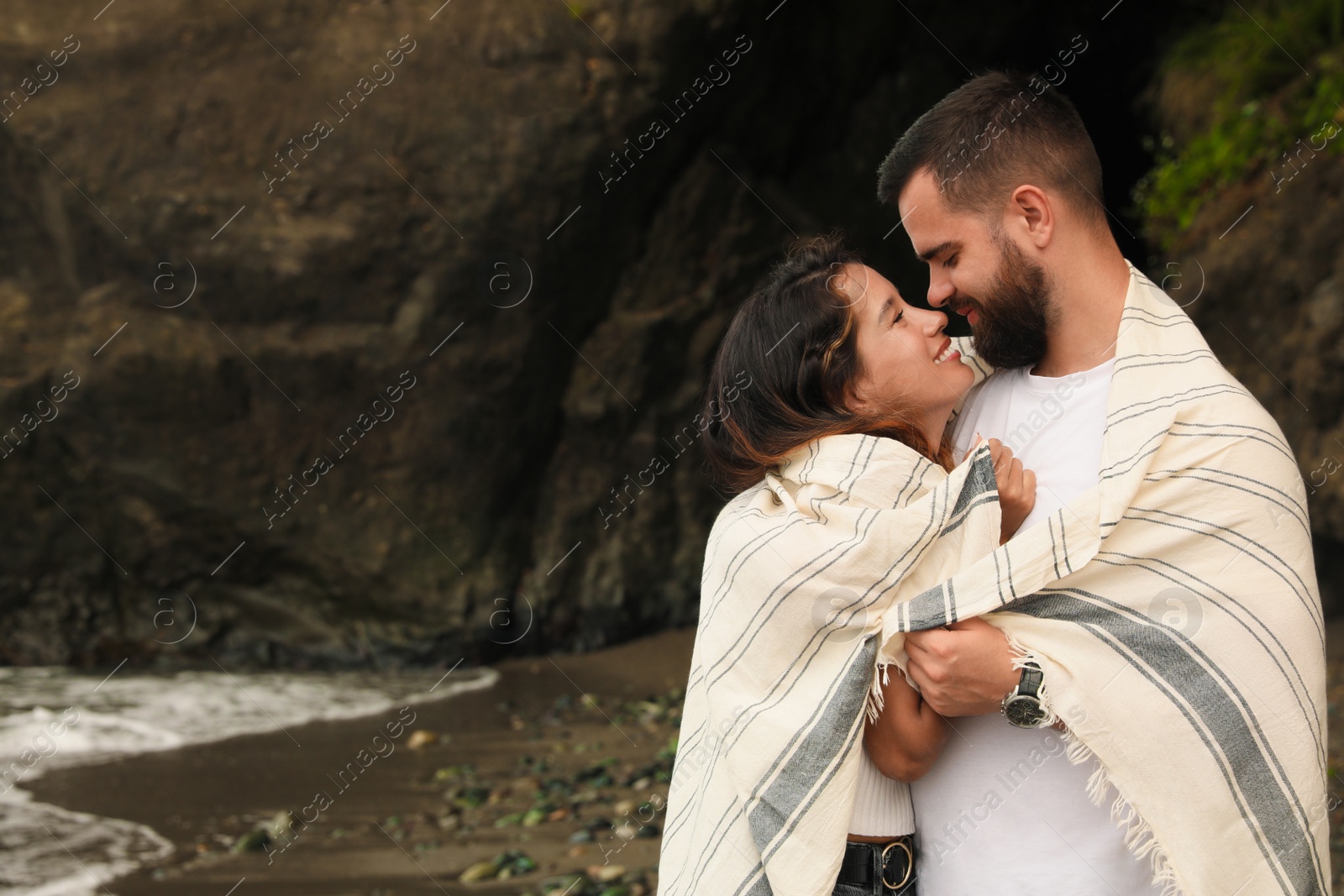 Photo of Happy young couple with blanket on beach near sea. Space for text