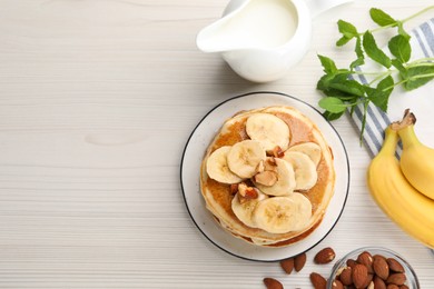 Tasty pancakes with sliced banana served on white wooden table, flat lay. Space for text