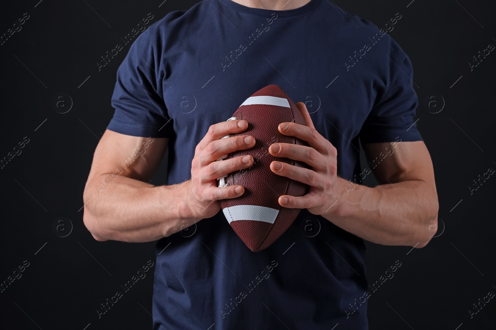Photo of Athletic man with American football ball on black background, closeup
