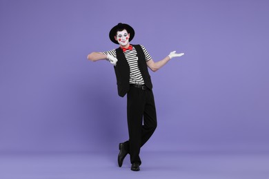 Photo of Funny mime artist in hat posing on purple background