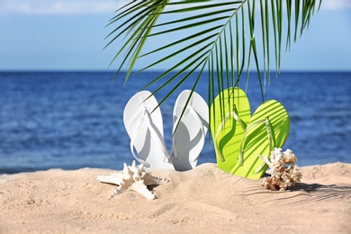 Photo of Composition with bright flip flops on sand near sea in summer. Beach accessories