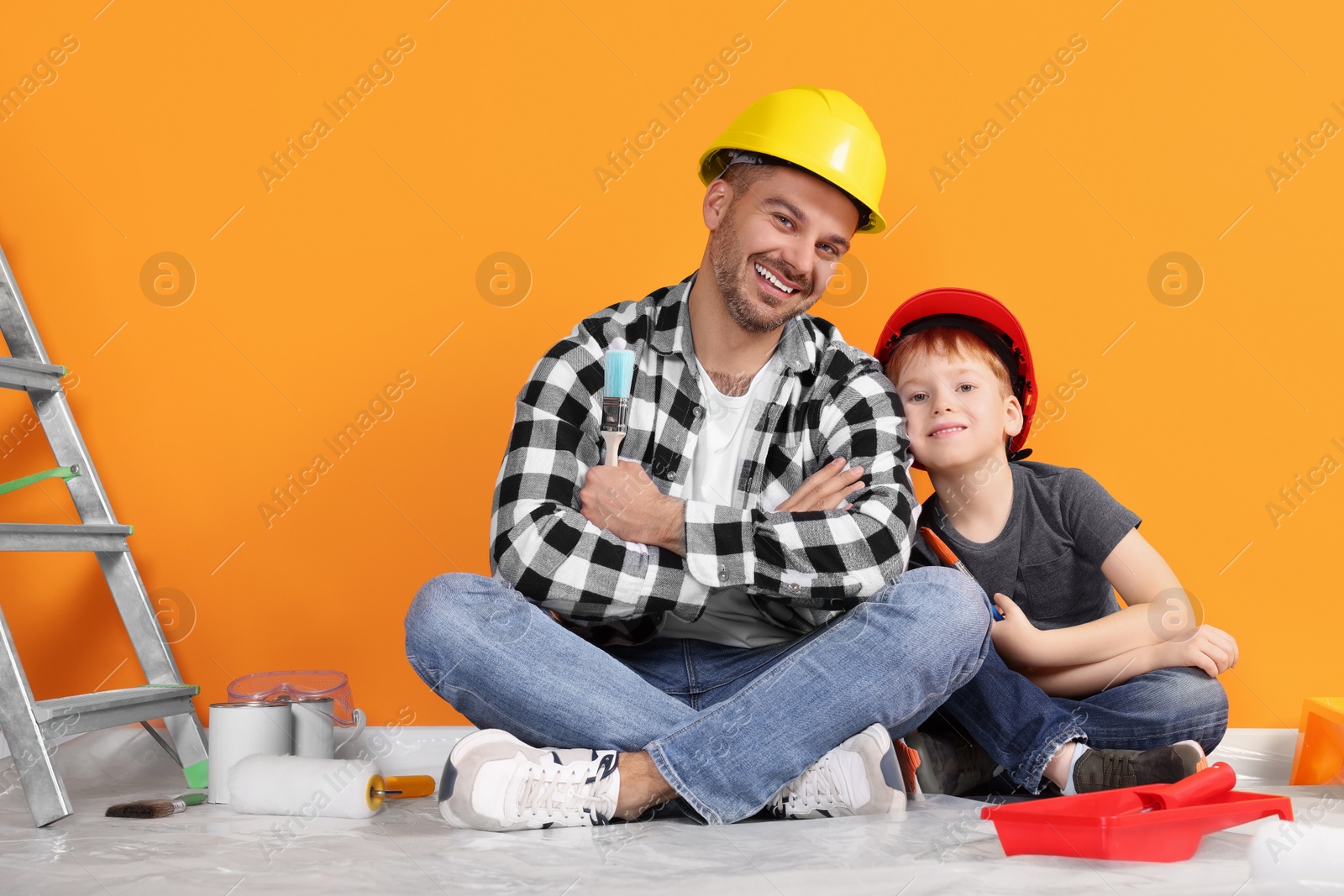 Photo of Father and son with repair tools near orange wall