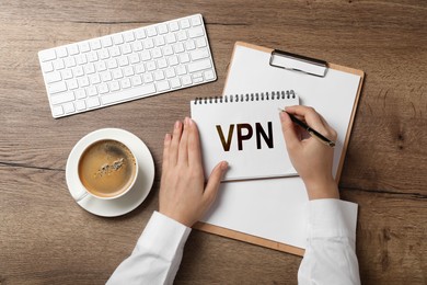 Image of Woman writing acronym VPN in notebook at wooden table, top view. Secure network connection