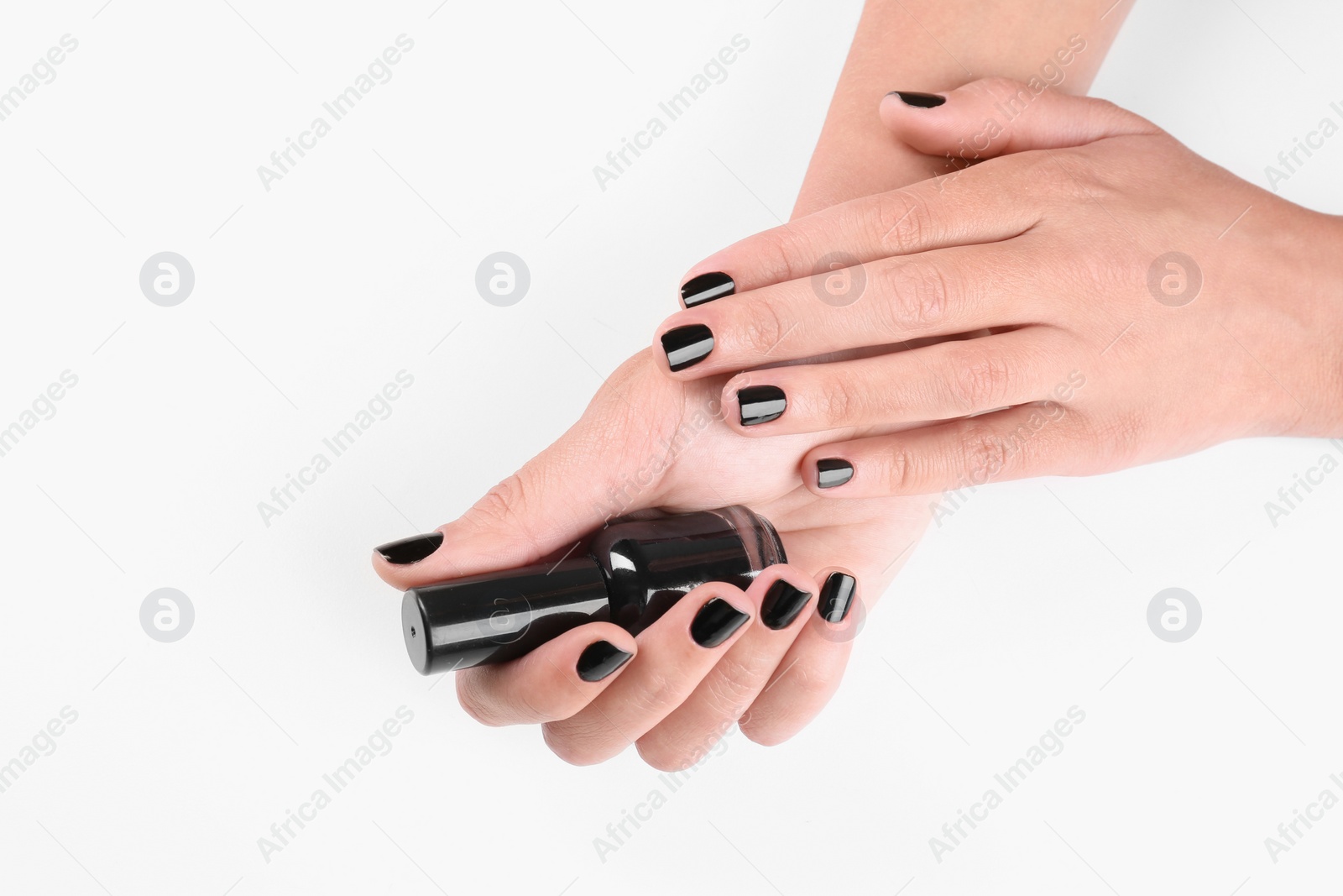 Photo of Woman with black manicure holding nail polish bottle on white background, closeup