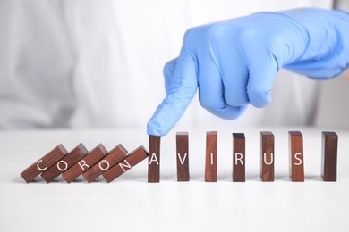 Photo of Doctor stopping domino effect at white table, closeup. Prevent spreading of coronavirus