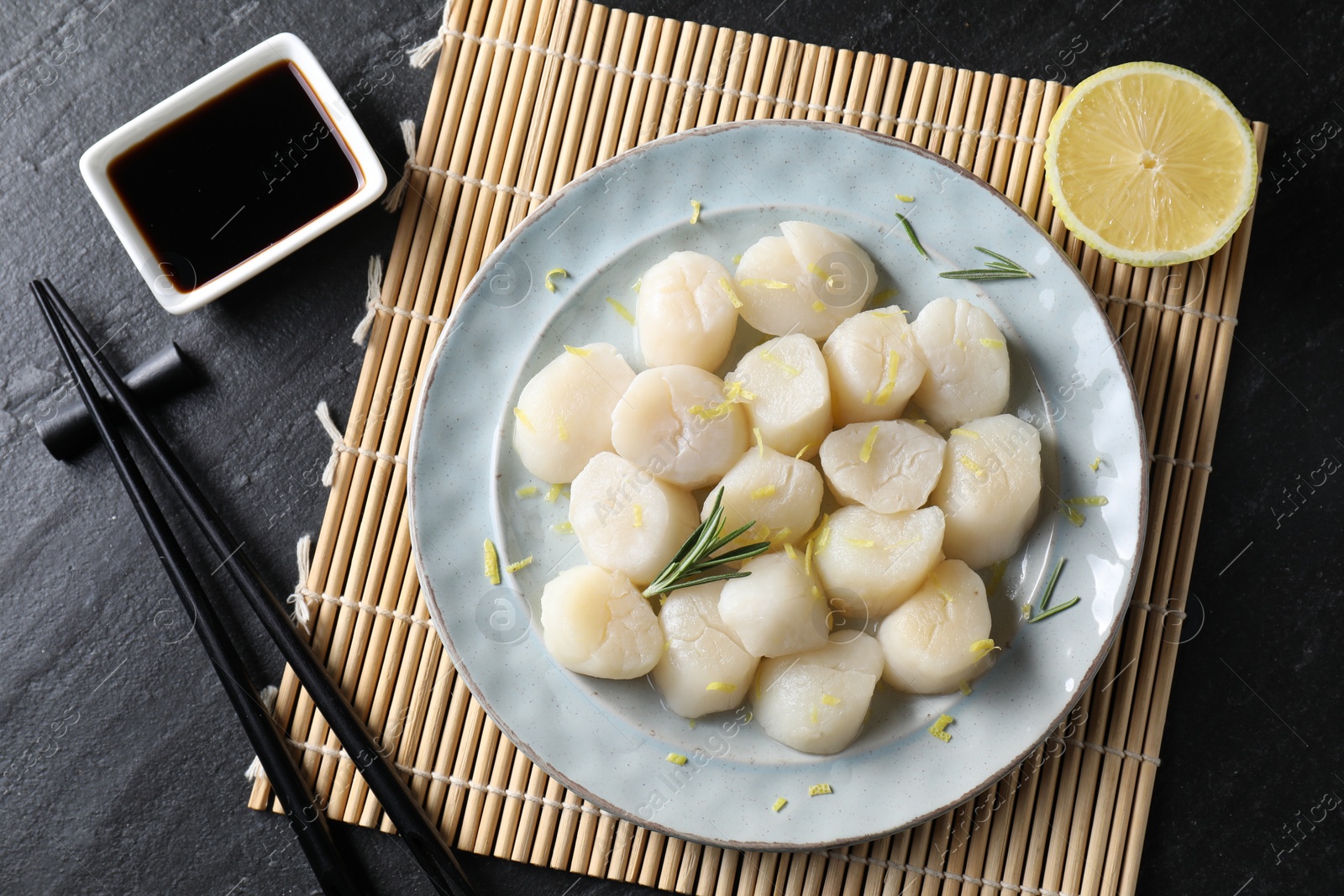 Photo of Raw scallops with lemon, rosemary and soy sauce on dark textured table, flat lay