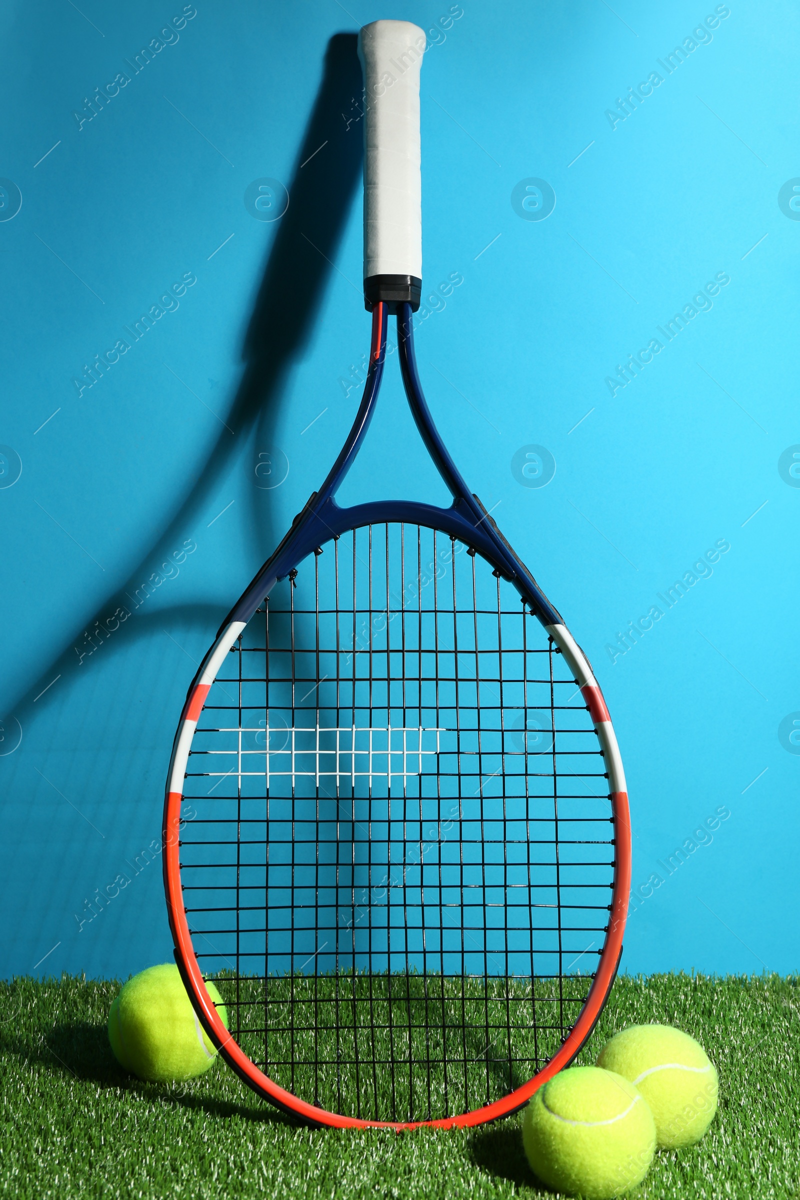 Photo of Tennis racket and balls on green grass against light blue background. Sports equipment