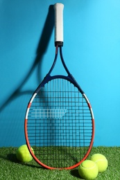 Tennis racket and balls on green grass against light blue background. Sports equipment