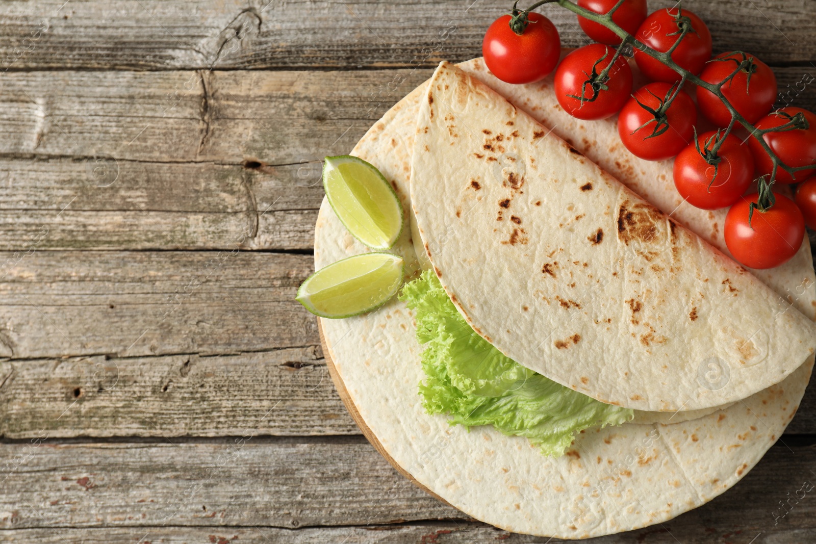 Photo of Tasty homemade tortillas, tomatoes, lime and lettuce on wooden table, top view. Space for text