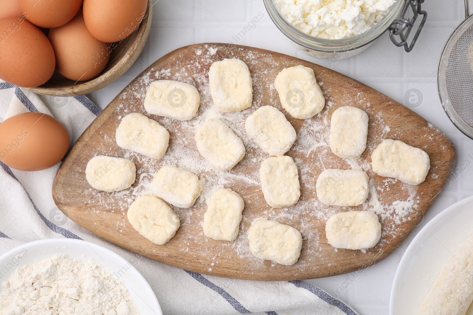 Photo of Making lazy dumplings. Board with cut dough and ingredients on white tiled table, flat lay