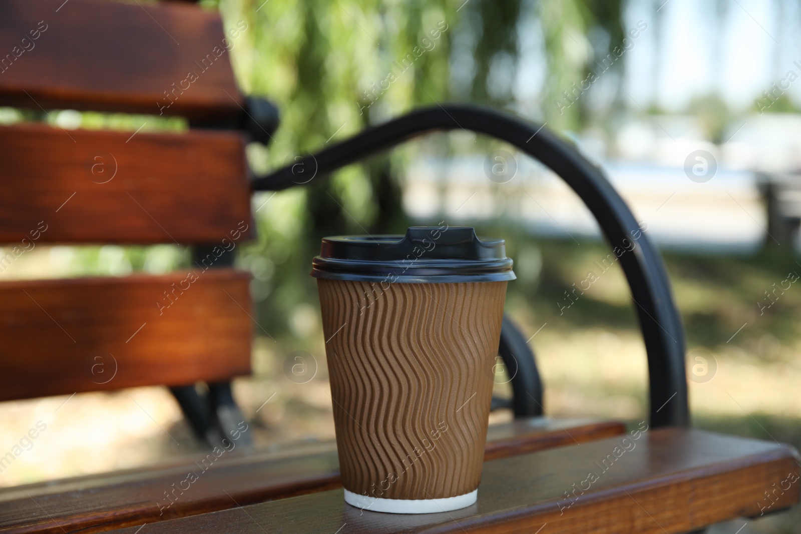 Photo of Takeaway cardboard coffee cup with plastic lid on wooden bench outdoors