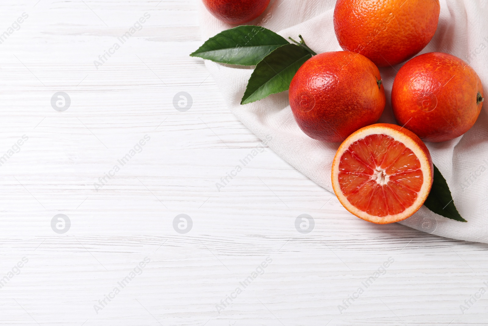 Photo of Whole and cut red oranges on white wooden table. Space for text