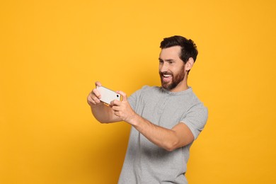 Photo of Emotional man playing game on smartphone against yellow background