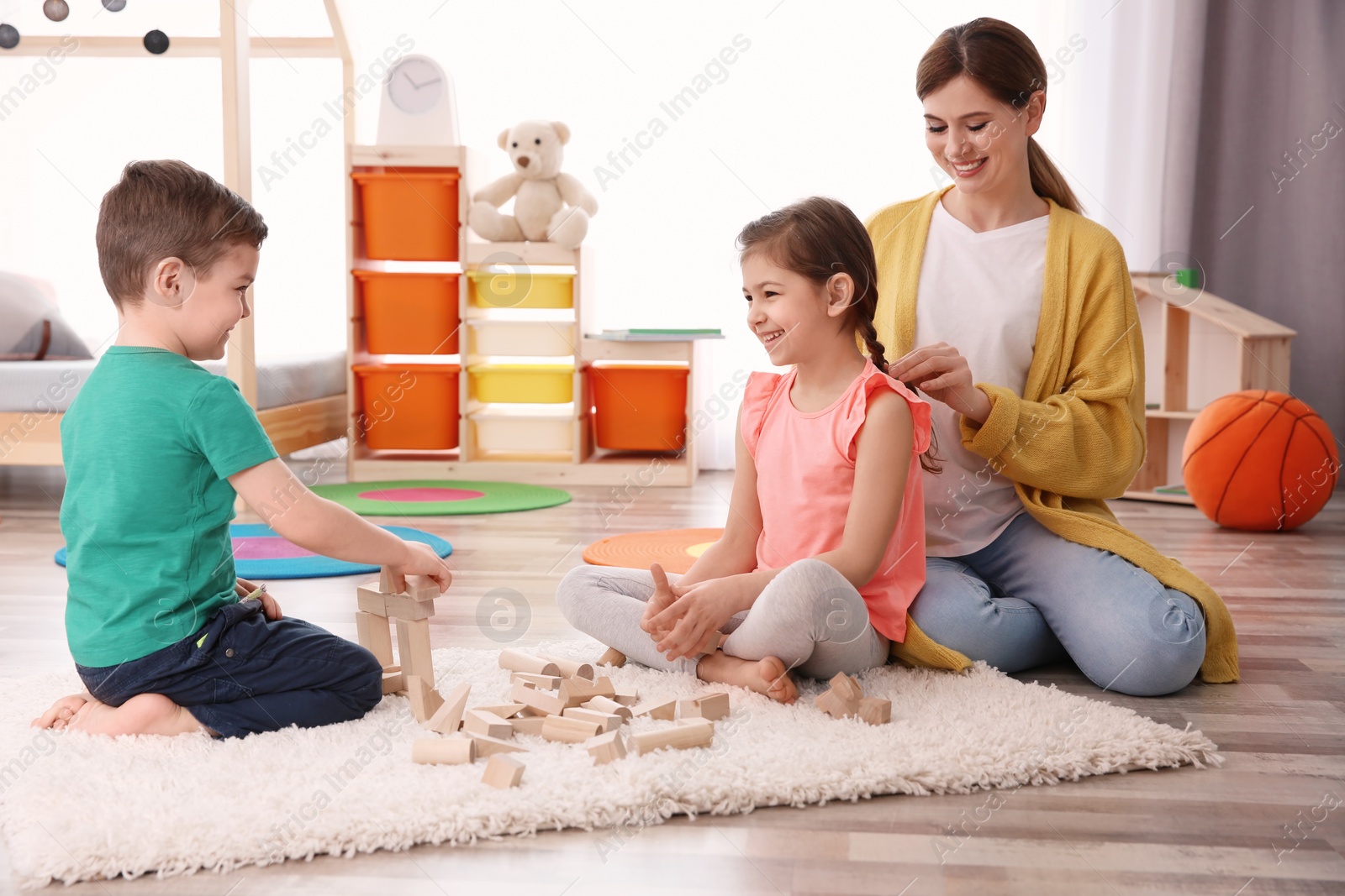 Photo of Little children playing while nanny braiding girl's hair at home