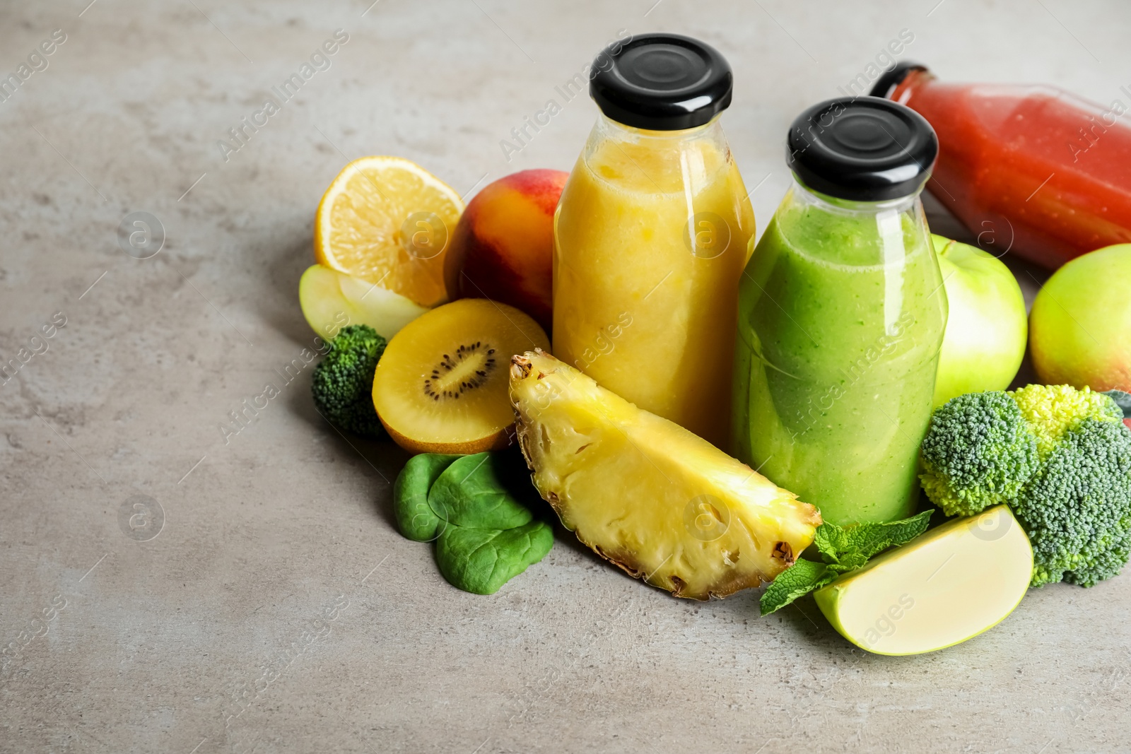 Photo of Bottles of delicious juices and fresh fruits on grey table