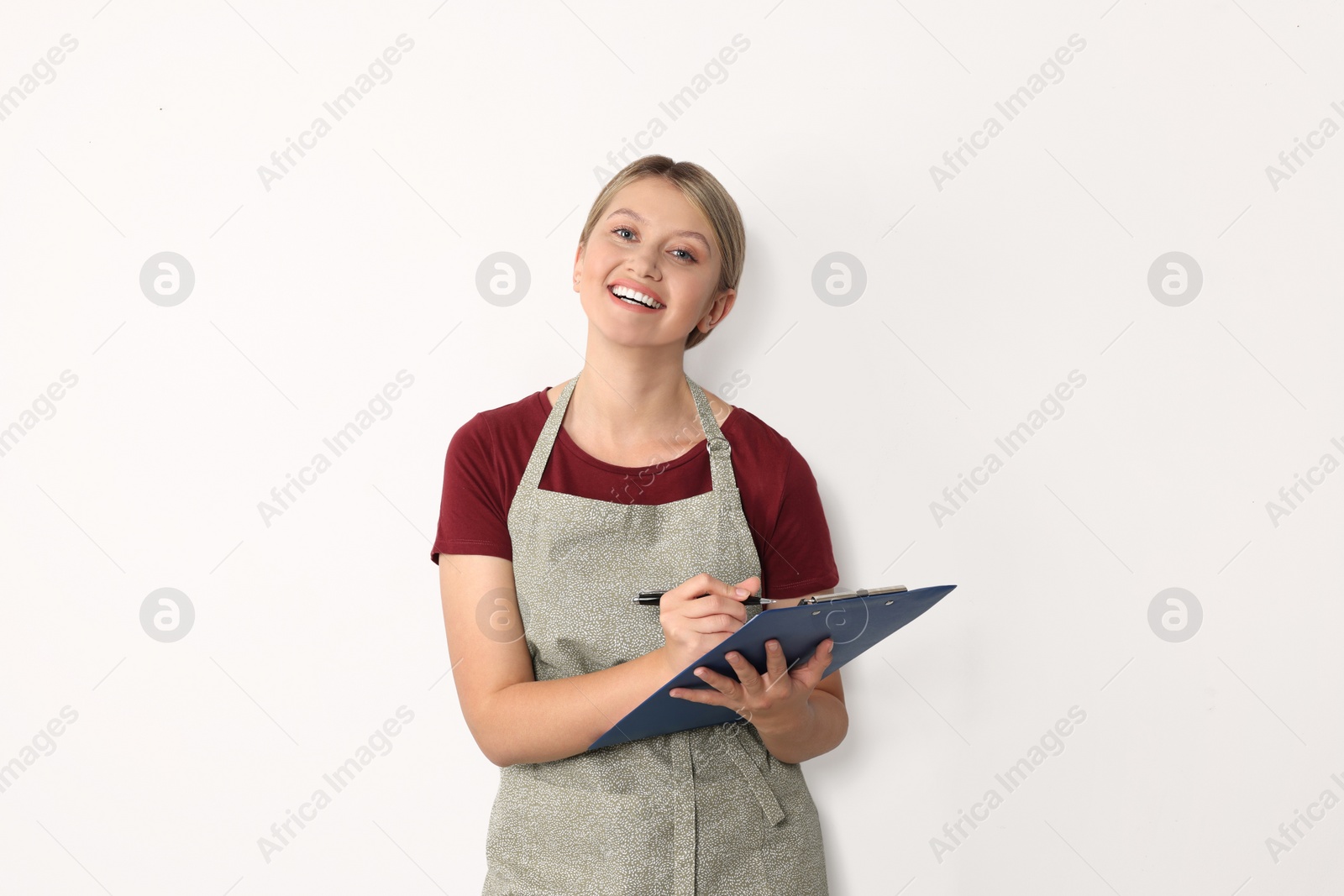 Photo of Beautiful young woman in clean apron with clipboard on light grey background