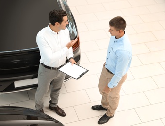 Photo of Young salesman working with client in modern car dealership, above view