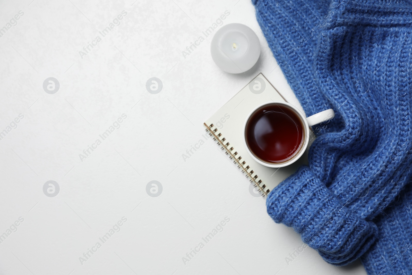 Ceramic mug with aromatic tea, blue knitted sweater, notebook and candle on white background, flat lay. Space for text Photo of Ceramic mug with aromatic tea, blue knitted sweater, notebook and candle on white background, flat lay. Space for text