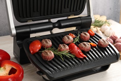 Photo of Electric grill with vegetables, meat balls and rosemary on wooden table