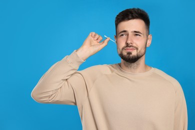 Young man cleaning ear with cotton swab on light blue background