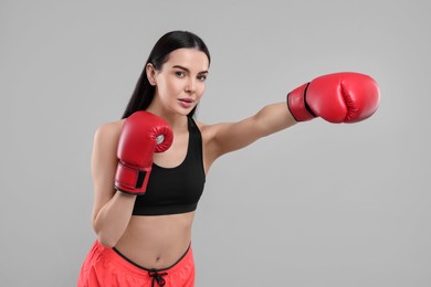 Beautiful woman in boxing gloves training on grey background