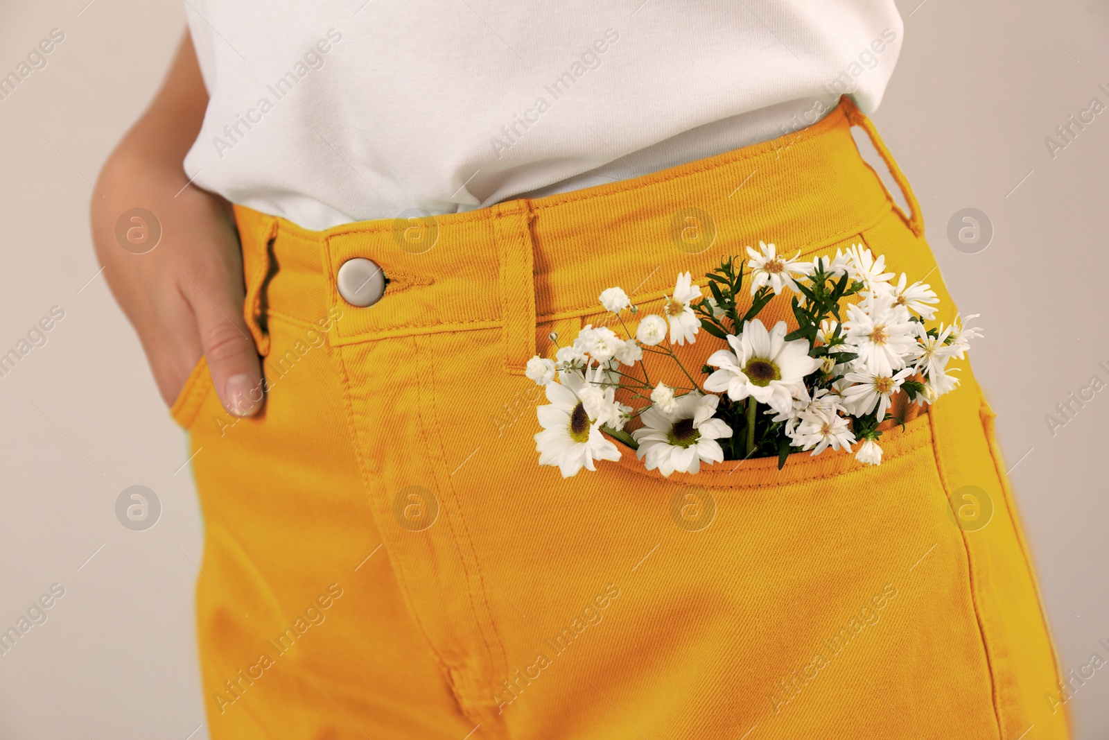 Image of Woman with beautiful tender flowers in pocket of orange jeans on light background, closeup