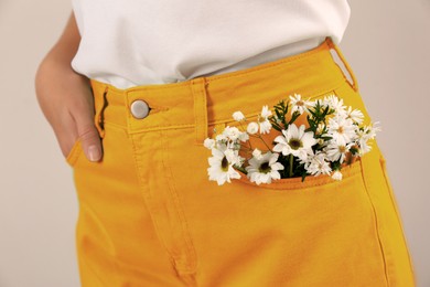 Woman with beautiful tender flowers in pocket of orange jeans on light background, closeup