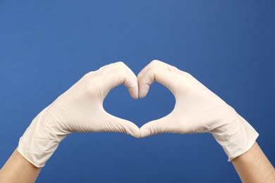 Photo of Person in medical gloves showing heart gesture on blue background, closeup of hands
