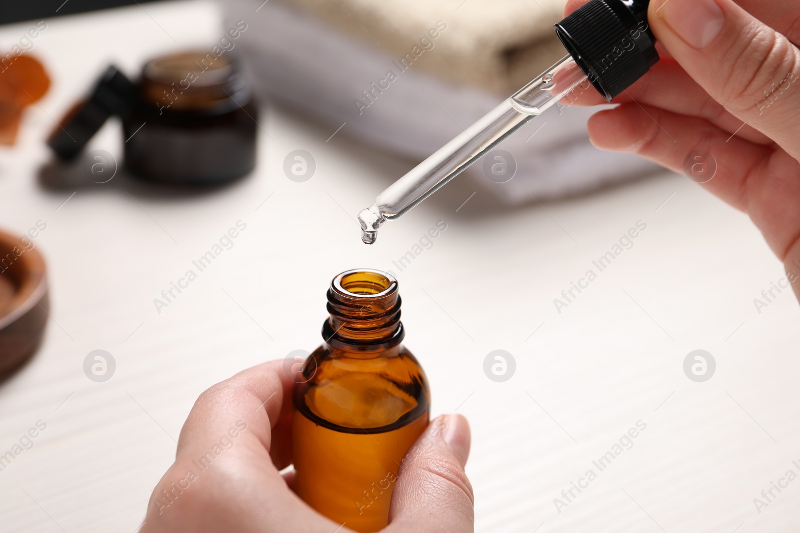 Photo of Woman with bottle of cosmetic serum and pipette at white table, closeup