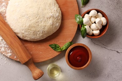 Photo of Pizza dough, products and rolling pin on gray textured table, flat lay