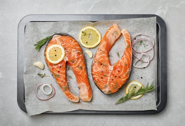 Baking dish with fresh raw salmon steaks and seasonings on gray background, top view