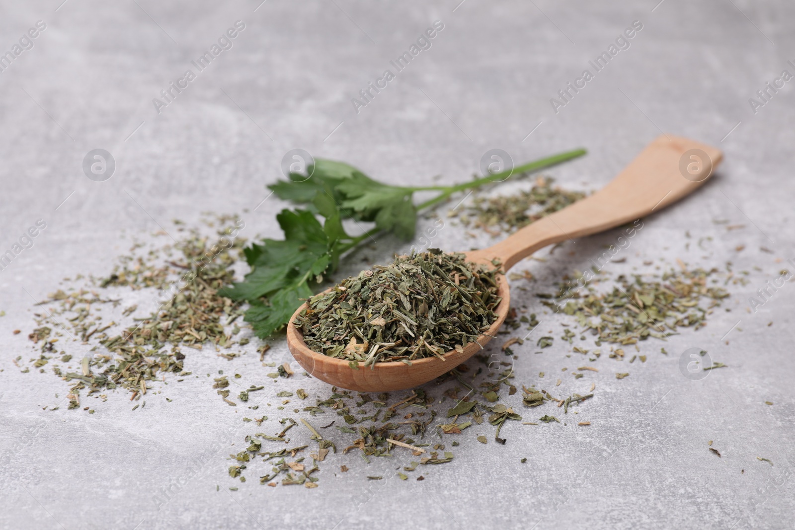 Photo of Wooden spoon with dried parsley and fresh leaves on light grey table