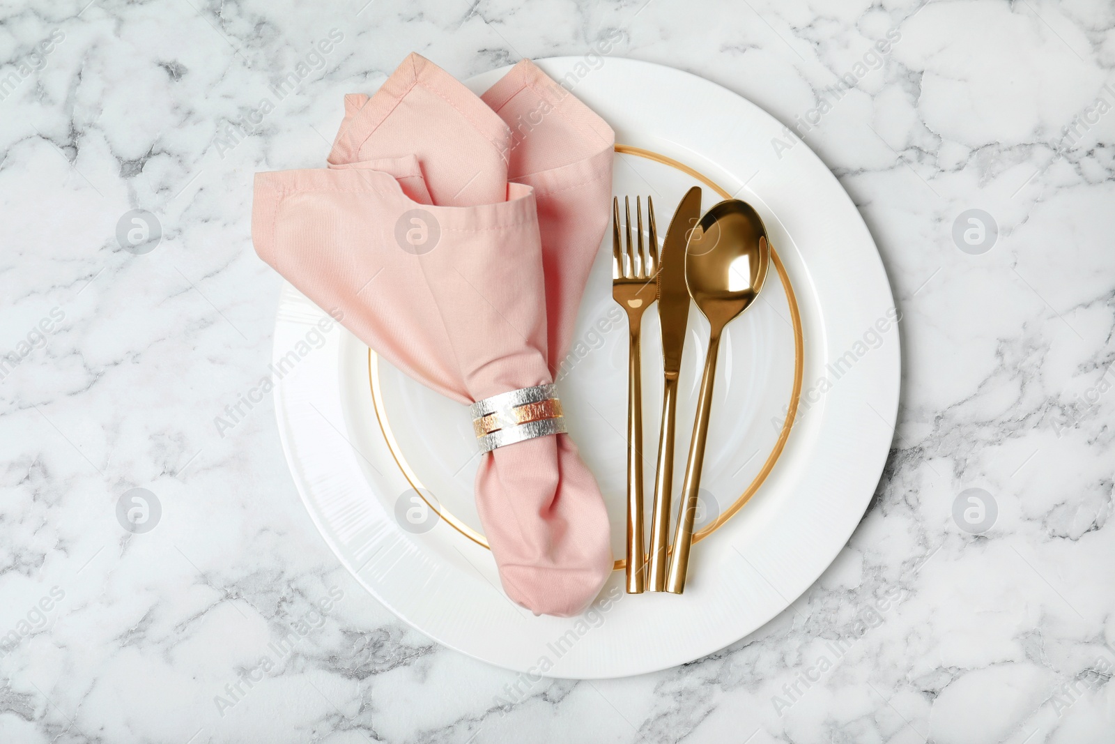 Photo of Plate with golden cutlery and napkin on marble background, top view. Festive dinner setting