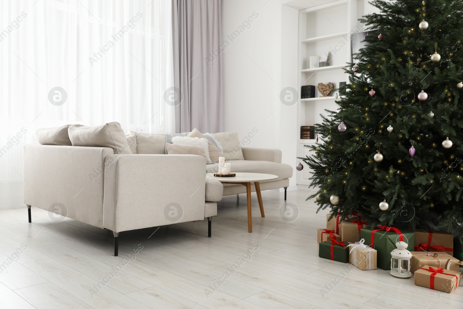 Photo of Beautifully wrapped gift boxes and lantern under Christmas tree in living room