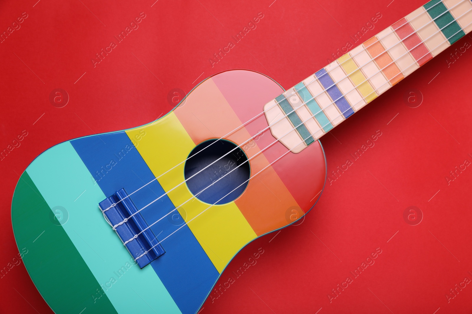 Photo of Colorful ukulele on red background, top view. String musical instrument