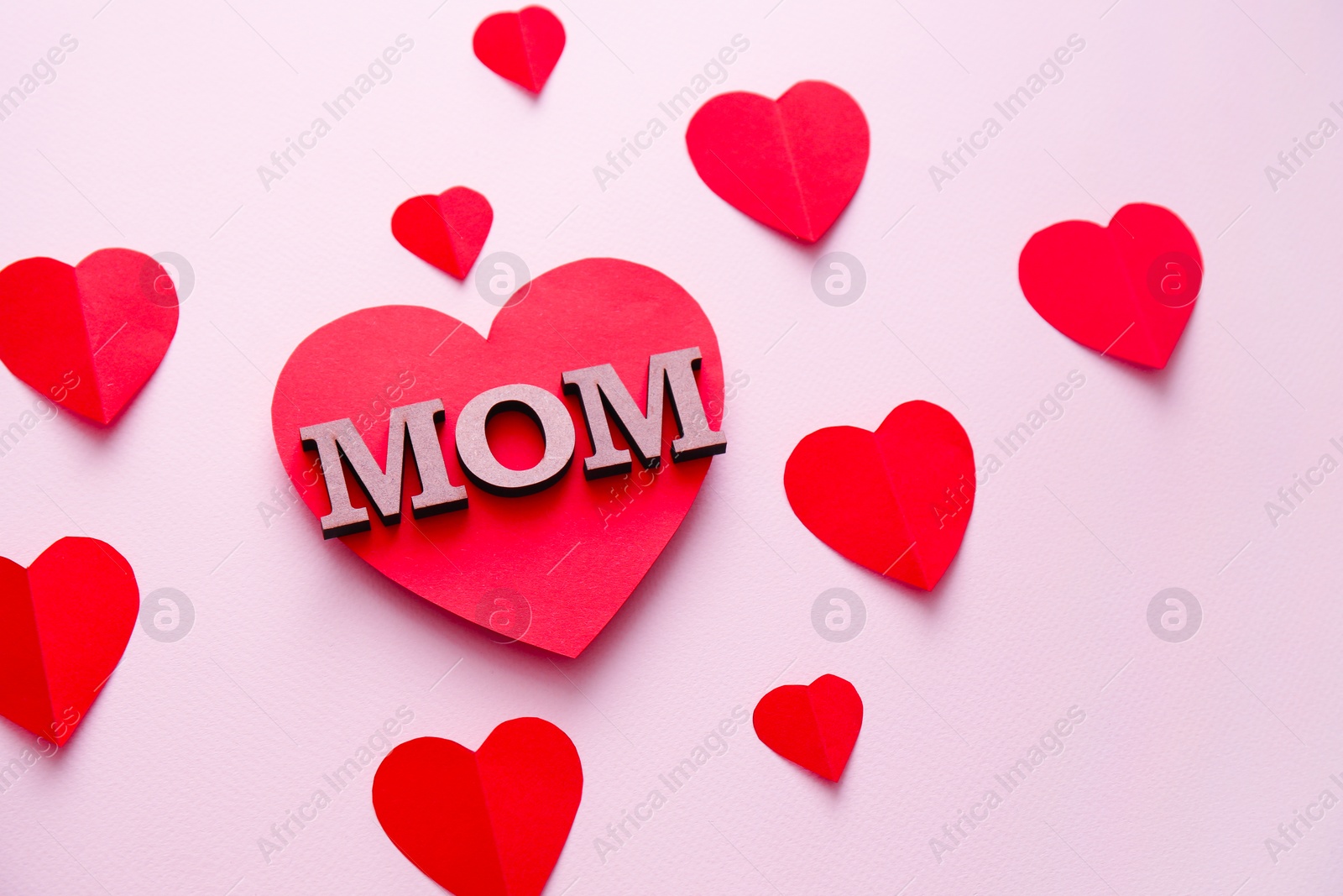 Photo of Beautiful composition with word MOM and paper hearts on color background. Happy Mother's Day