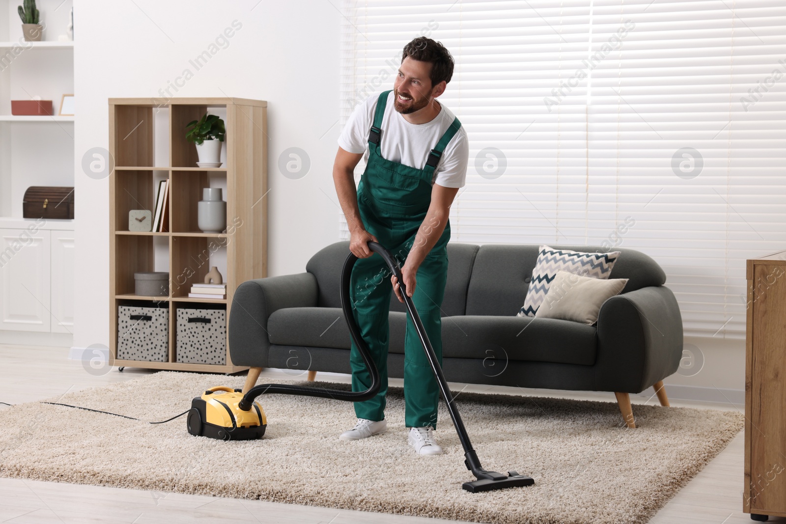 Photo of Dry cleaner's employee hoovering carpet with vacuum cleaner in room