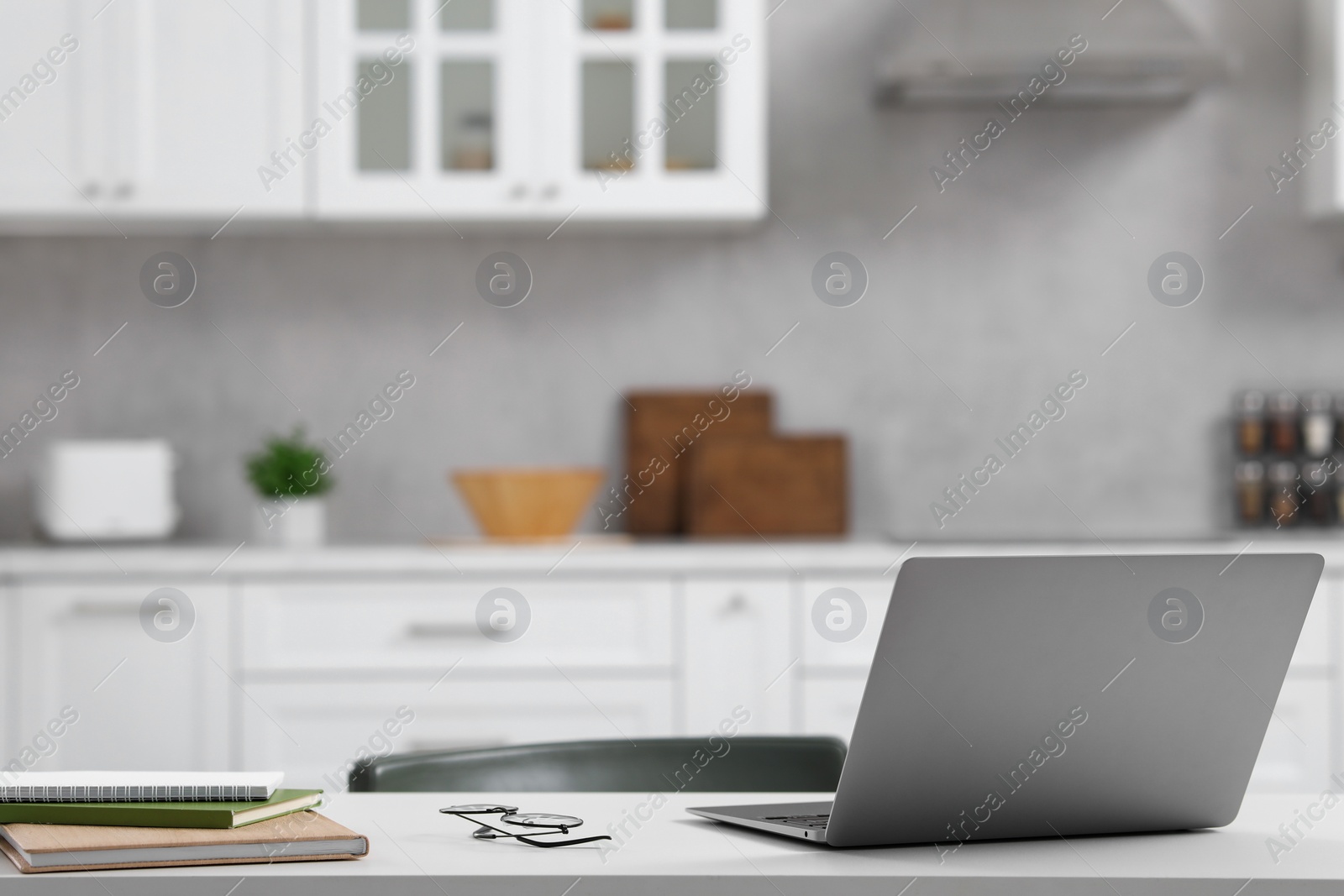 Photo of Home office. Laptop, glasses and stationery on white desk in kitchen, space for text