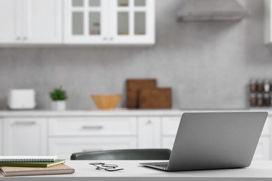 Photo of Home office. Laptop, glasses and stationery on white desk in kitchen, space for text