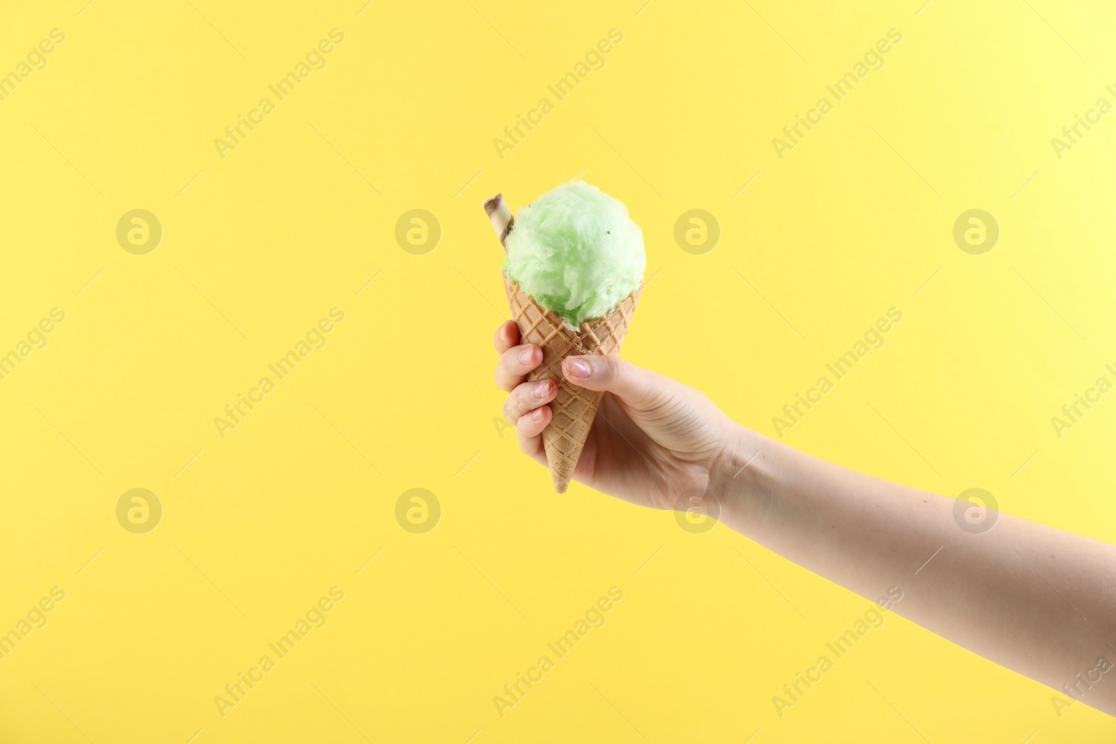 Photo of Woman holding waffle cone with cotton candy on yellow background, closeup